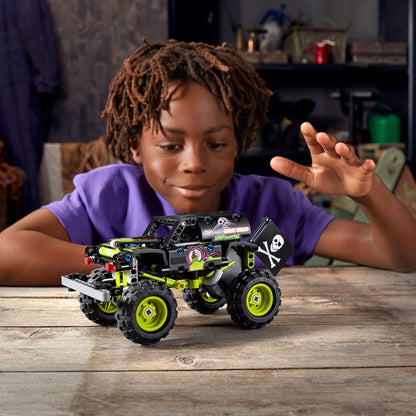 Child playing with LEGO Technic Monster Jam Grave Digger toy 42118 on a wooden table, showcasing creativity and fun.