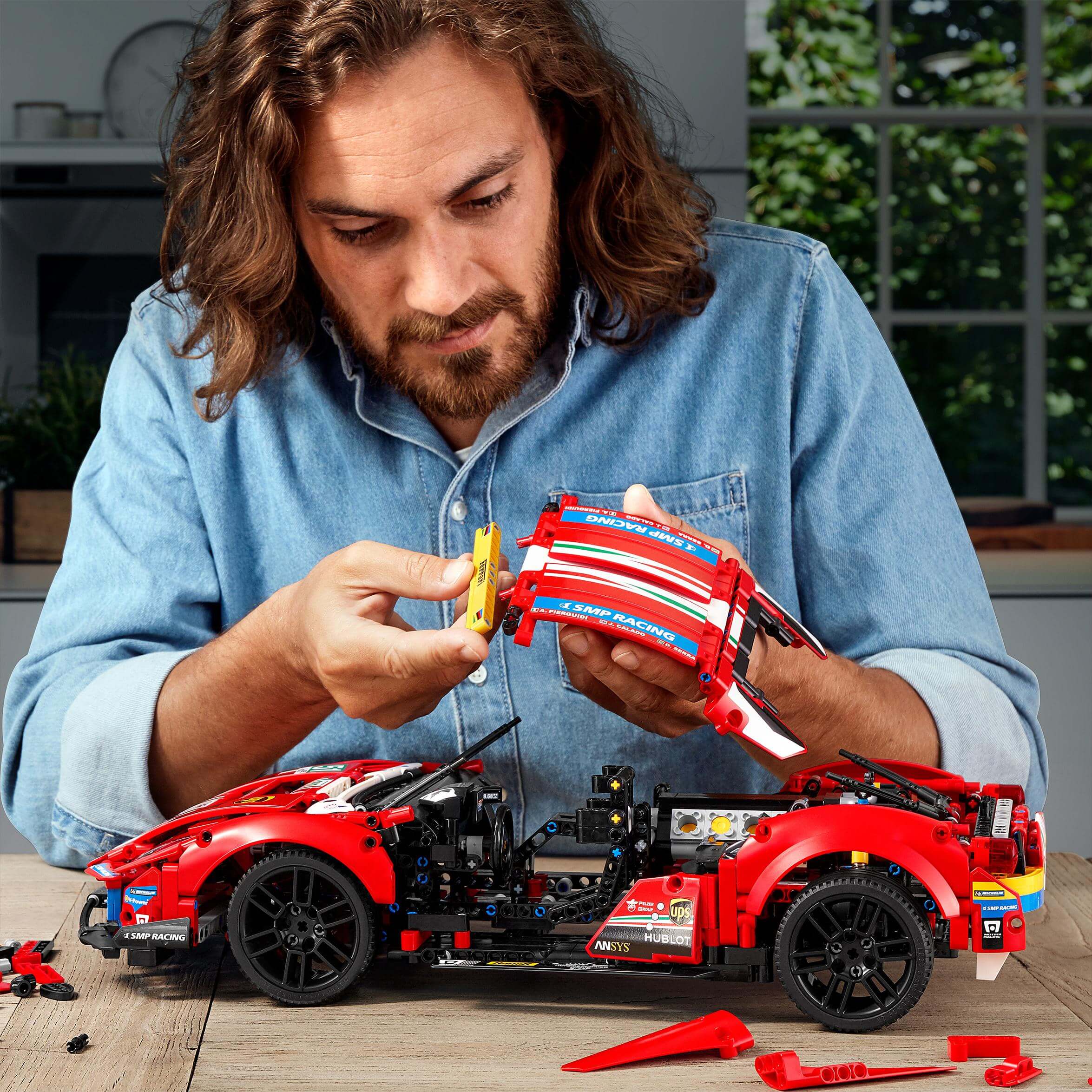 Person assembling LEGO® Technic Ferrari 488 GTE AF Corse #51 model on a table, surrounded by colorful building pieces.