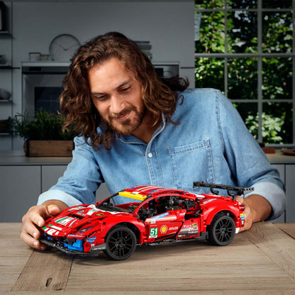 Person interacting with LEGO® Technic Ferrari 488 GTE AF Corse #51 set on a wooden table in a modern kitchen.