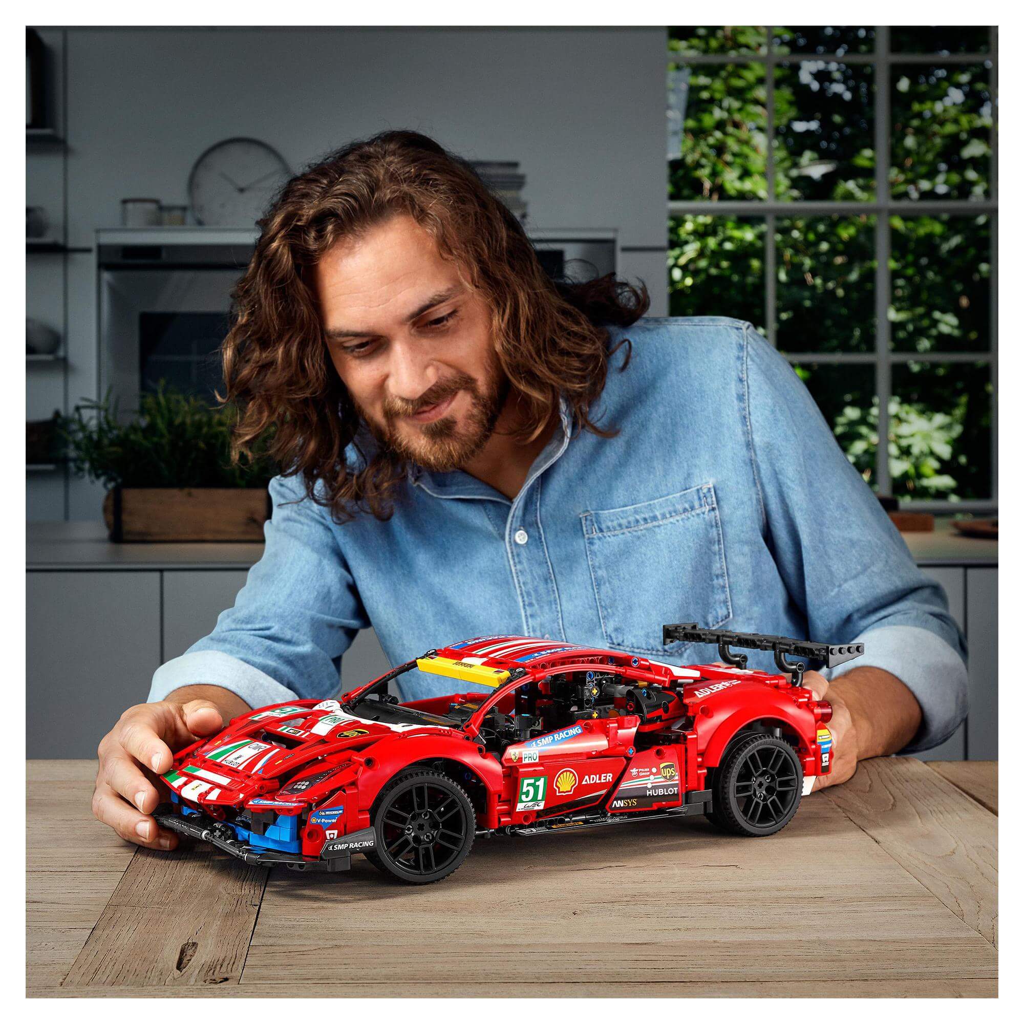 Adult male builds LEGO® Technic Ferrari 488 GTE AF Corse #51 model on a wooden table.