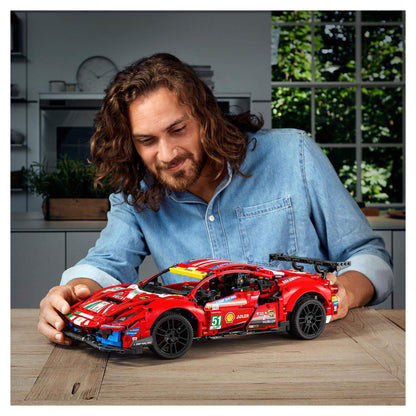 Adult male builds LEGO® Technic Ferrari 488 GTE AF Corse #51 model on a wooden table.