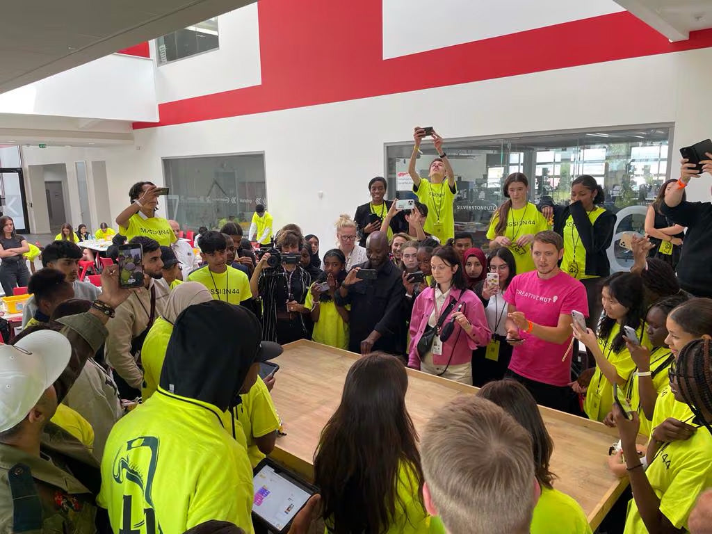 Group of youth in bright yellow shirts gathered around a table during an event, engaging with technology and each other.