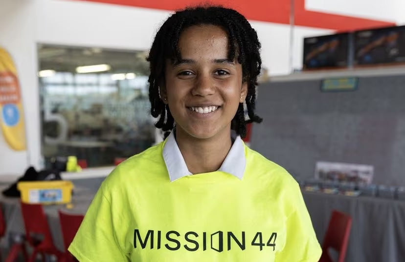 Smiling individual wearing a bright yellow Mission 44 shirt, standing inside a modern facility.