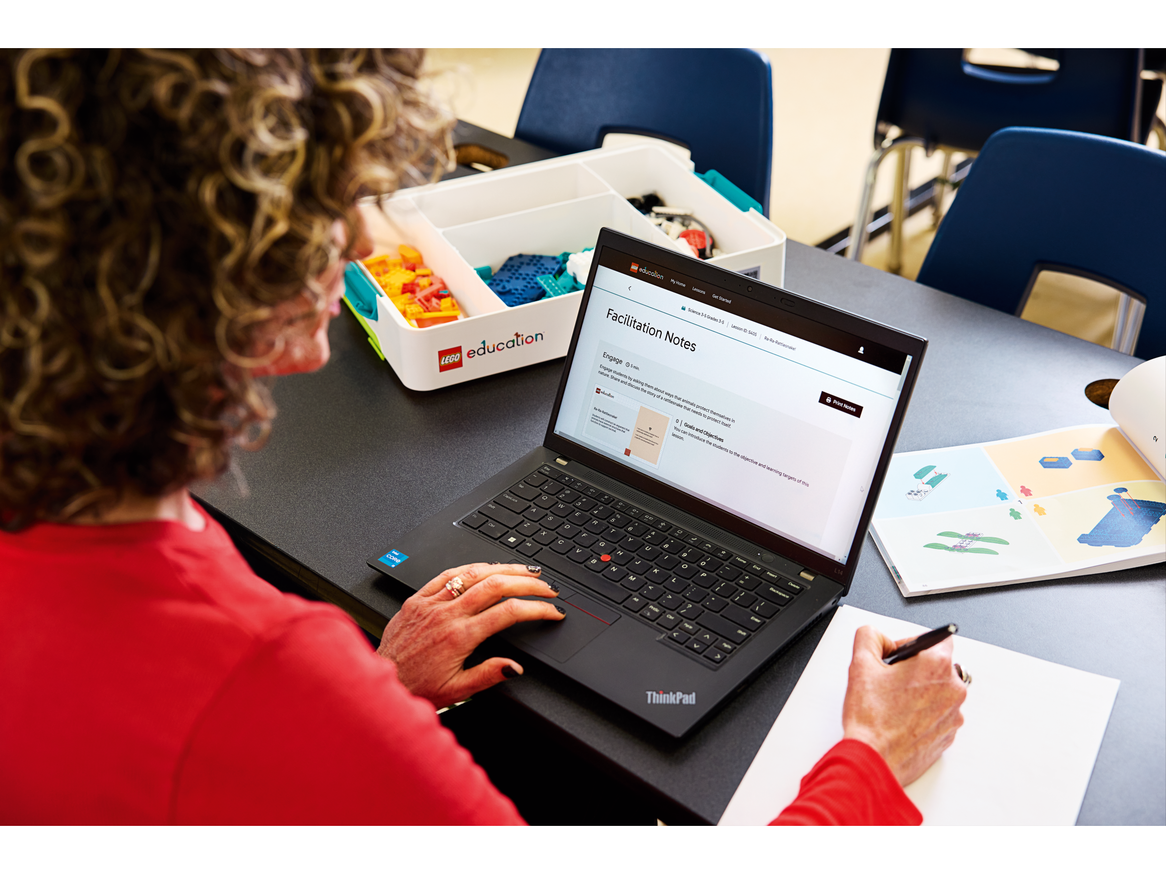Woman using a laptop for facilitation notes in a classroom setting with educational materials around.