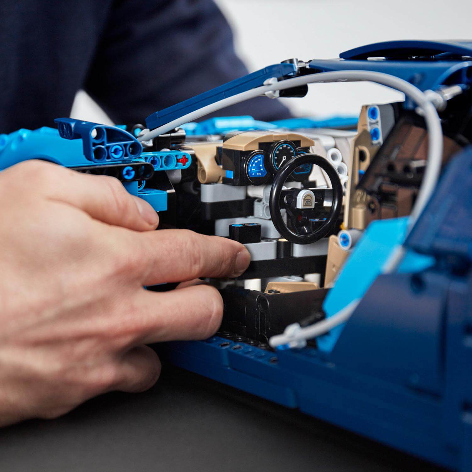 Close-up of a person assembling the interior of a blue toy car model, focusing on the dashboard and steering wheel.