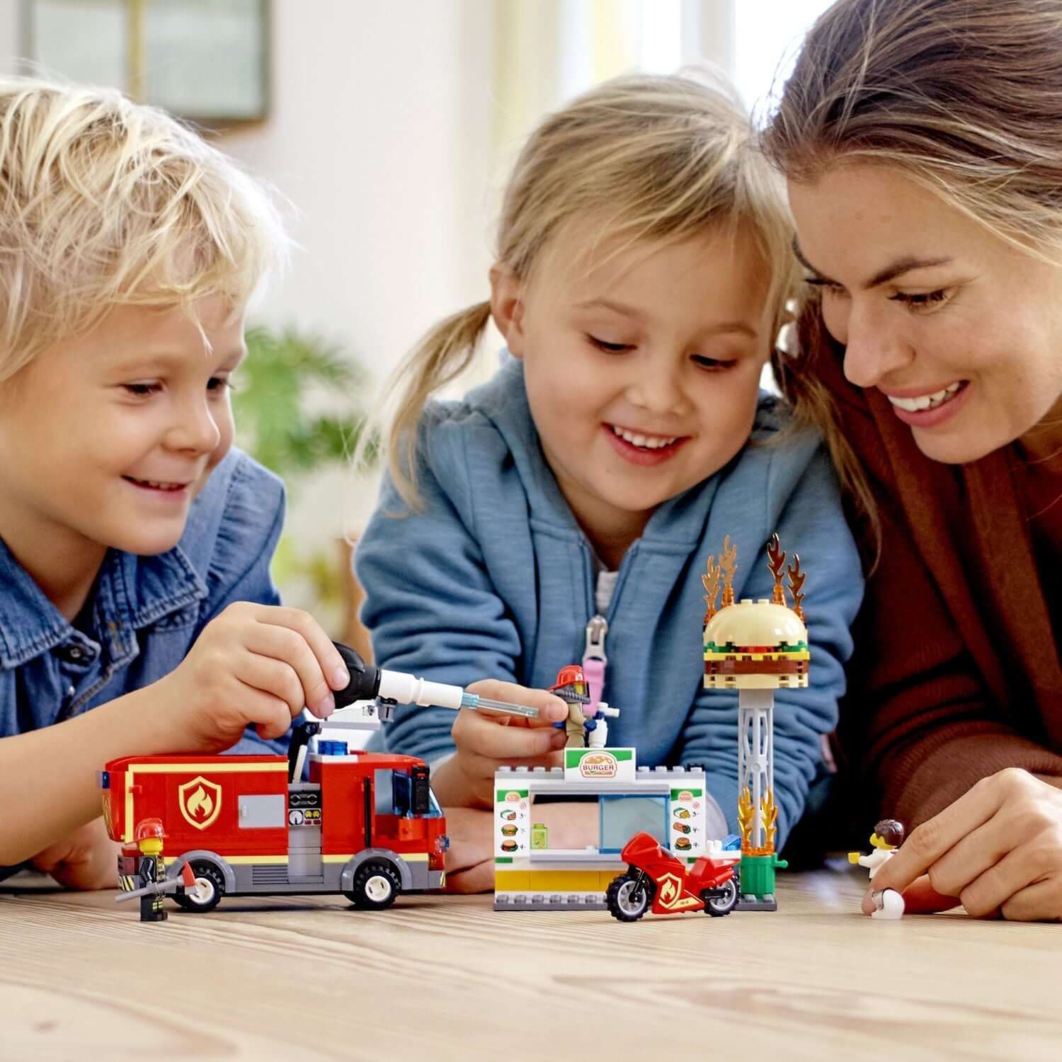 Children playing with LEGO® City Burger Bar Fire Rescue Engine toy set, engaging in imaginative play with their mother.