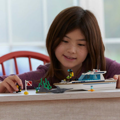Child playing with LEGO® City Diving Yacht set 60221, featuring a boat and diving accessories on a table.