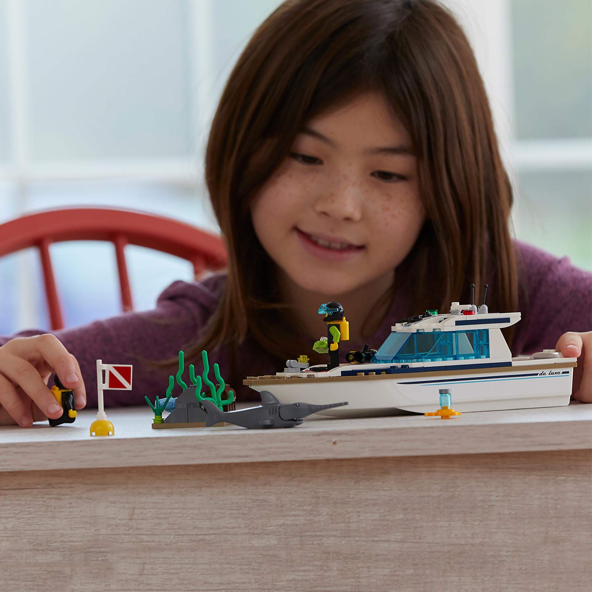 Girl playing with LEGO® City Diving Yacht set, exploring underwater adventure with divers and marine life.