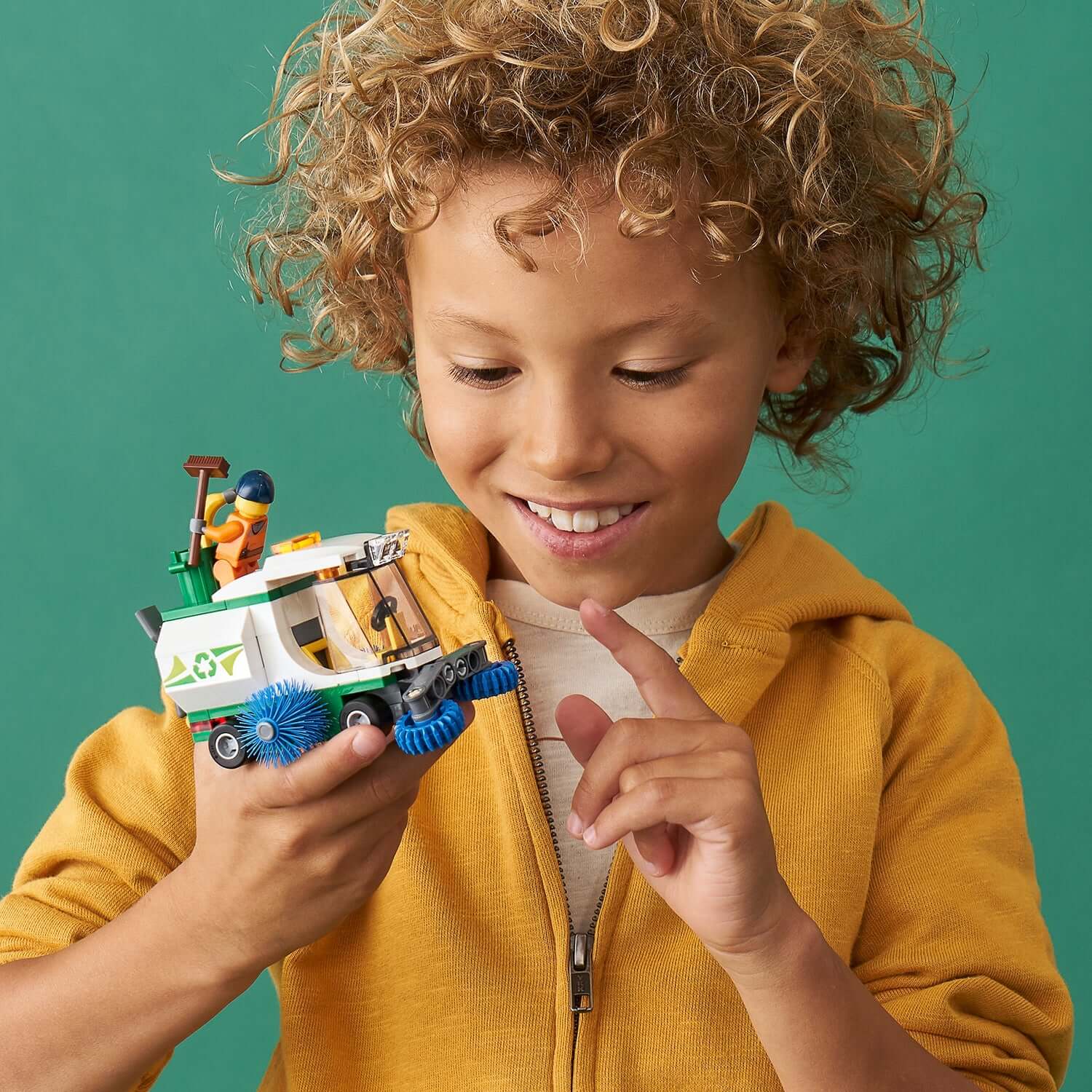 Child holding LEGO City Street Sweeper toy 60249 with a smiling expression, showcasing spinning brushes and minifigure.
