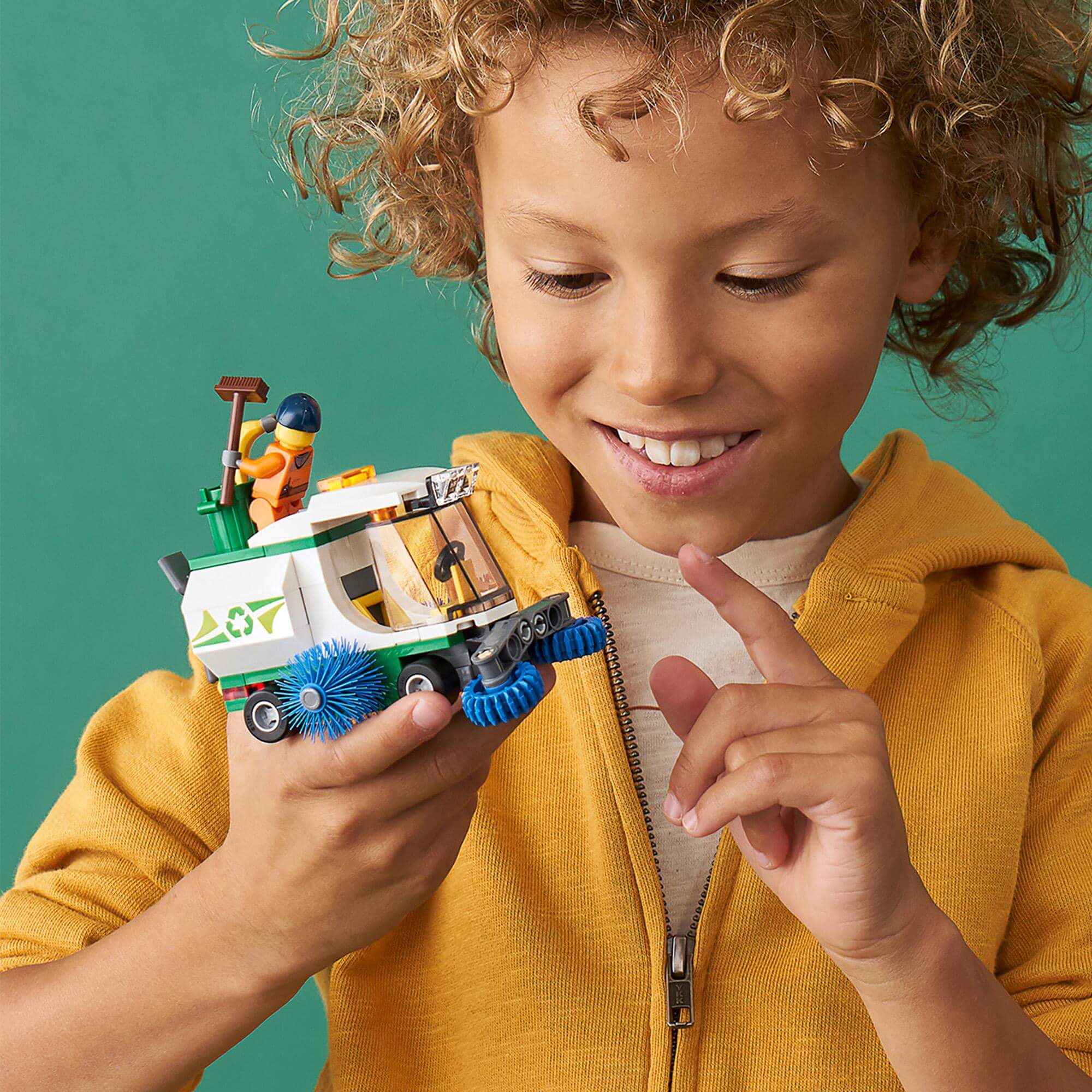 Child playing with LEGO® City Street Sweeper Toy 60249, featuring spinning brushes and a driver minifigure.