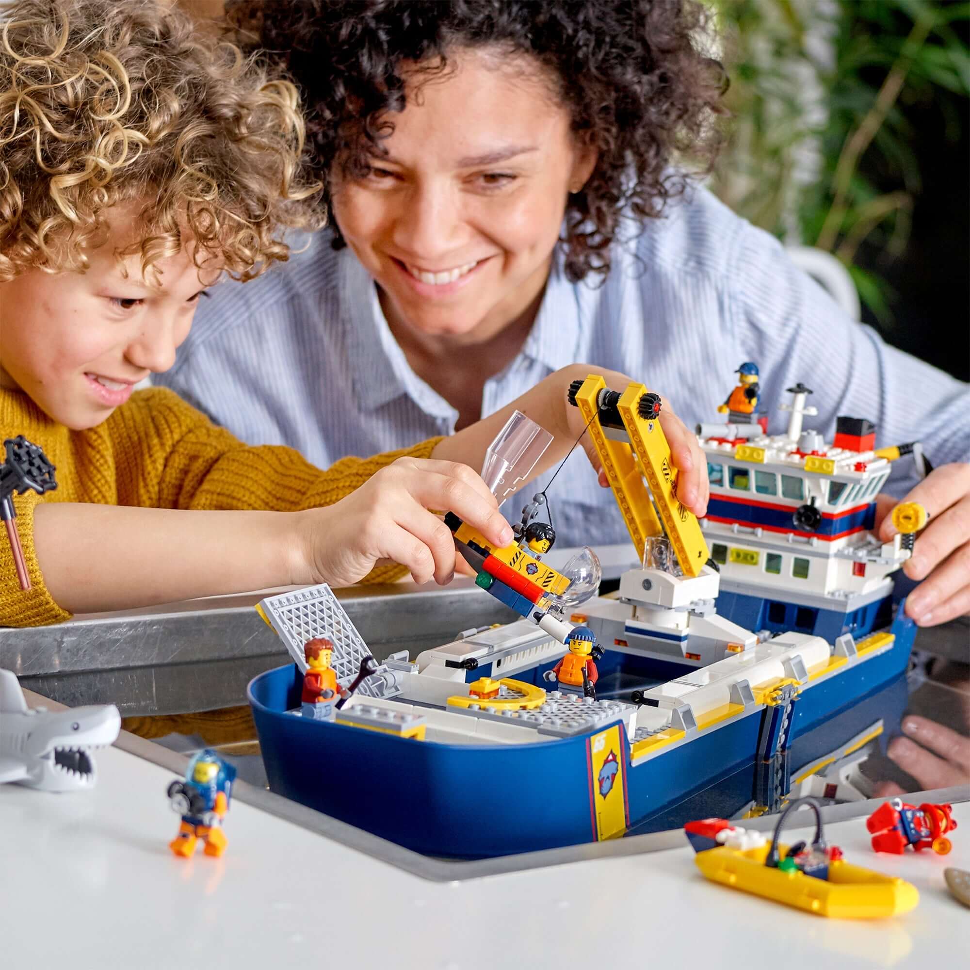 Child and adult play with LEGO® City Ocean Exploration Ship, featuring mini-figures and accessories for ocean adventure.