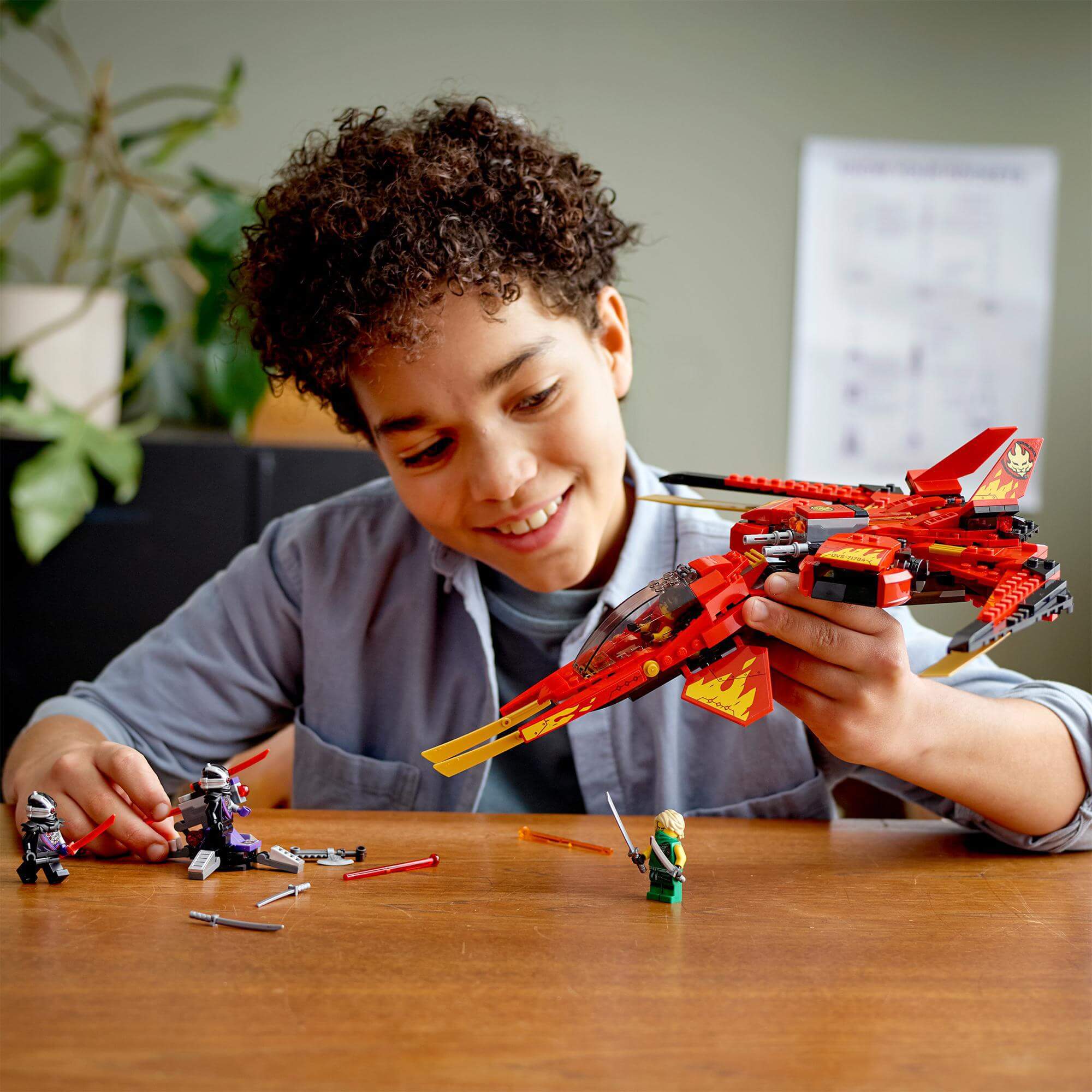 Child playing with LEGO NINJAGO Legacy Kai Fighter jet and minifigures in a creative setting.