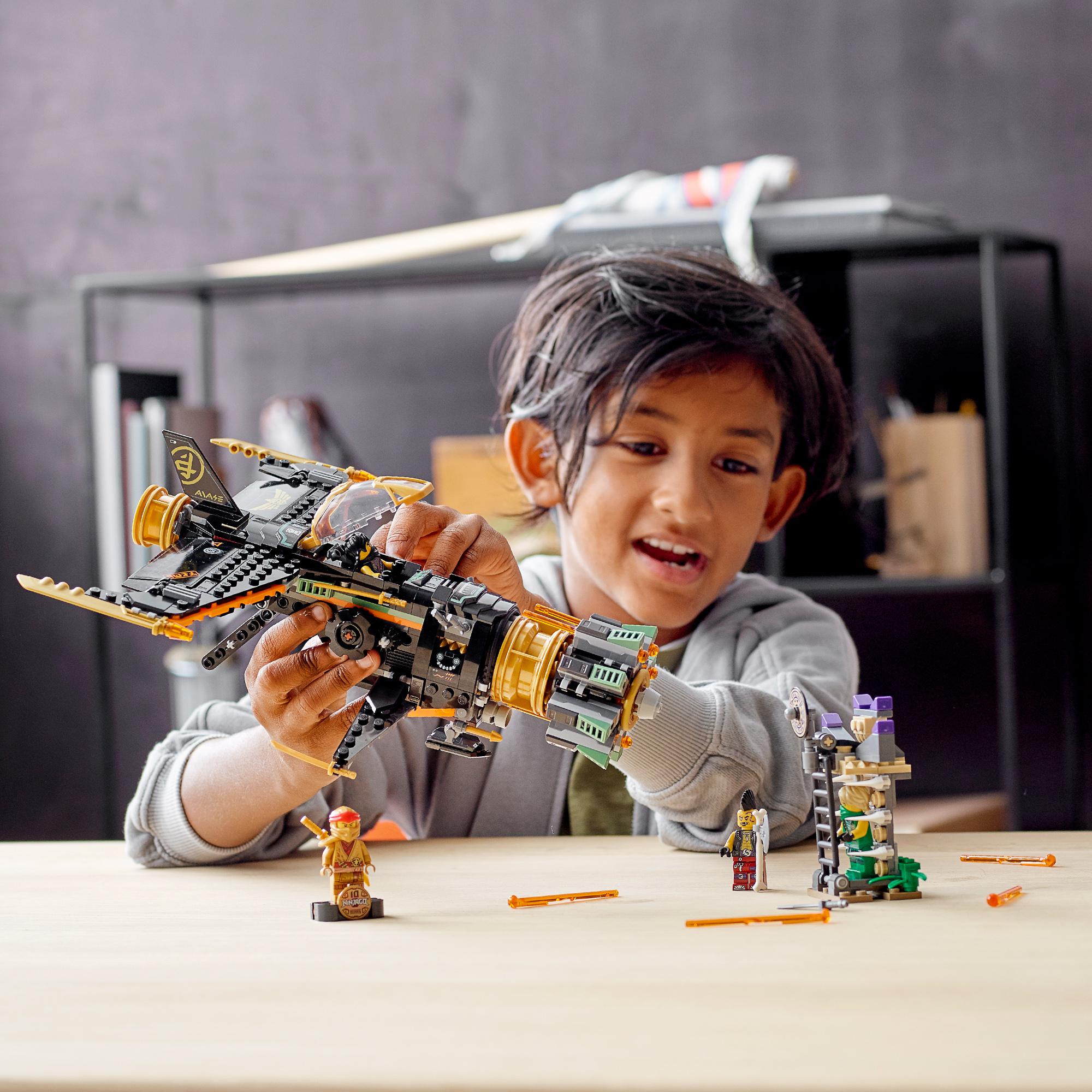 Boy playing with LEGO® NINJAGO Legacy Boulder Blaster Set 71736, featuring a toy airplane and ninja figures.