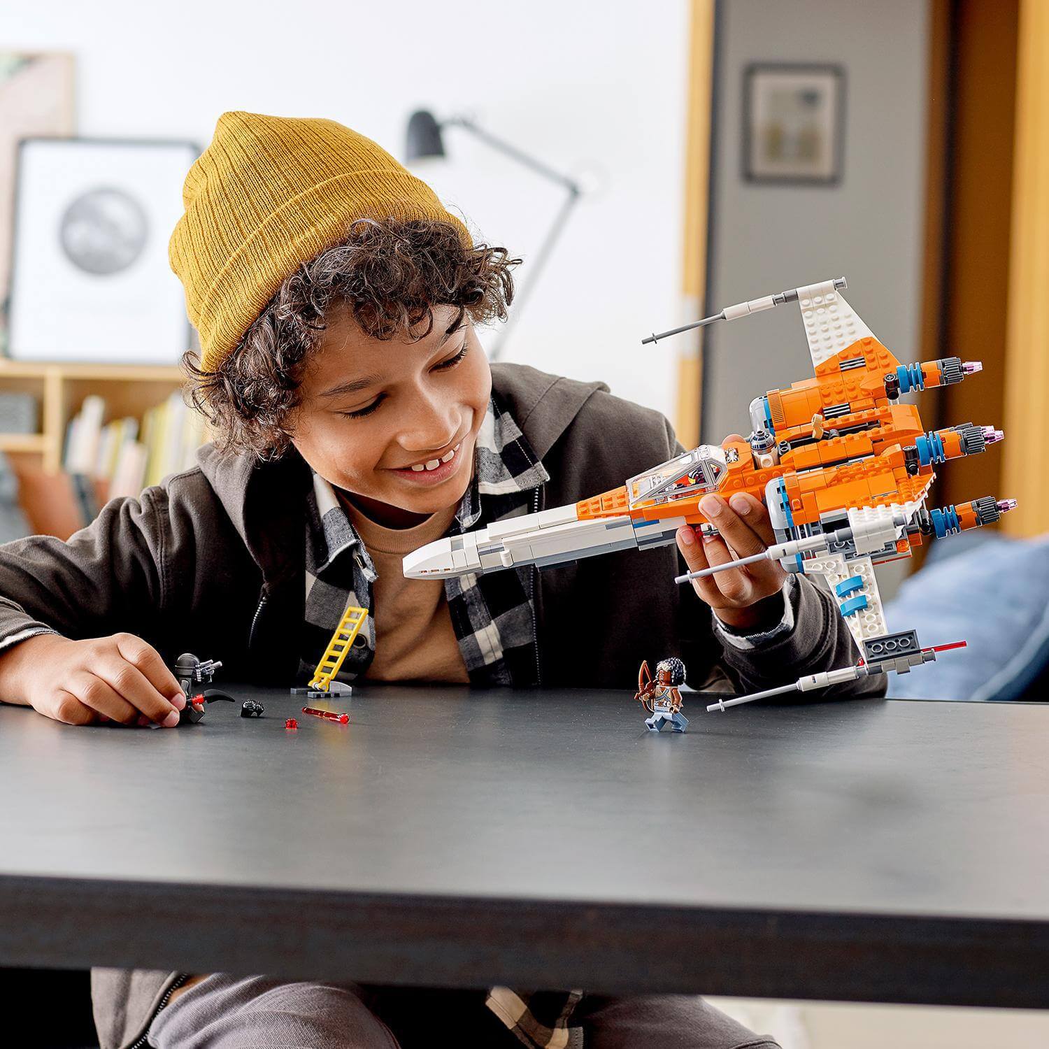 Child smiles while playing with LEGO Star Wars Poe Dameron's X-wing Fighter 75273 model on a table.