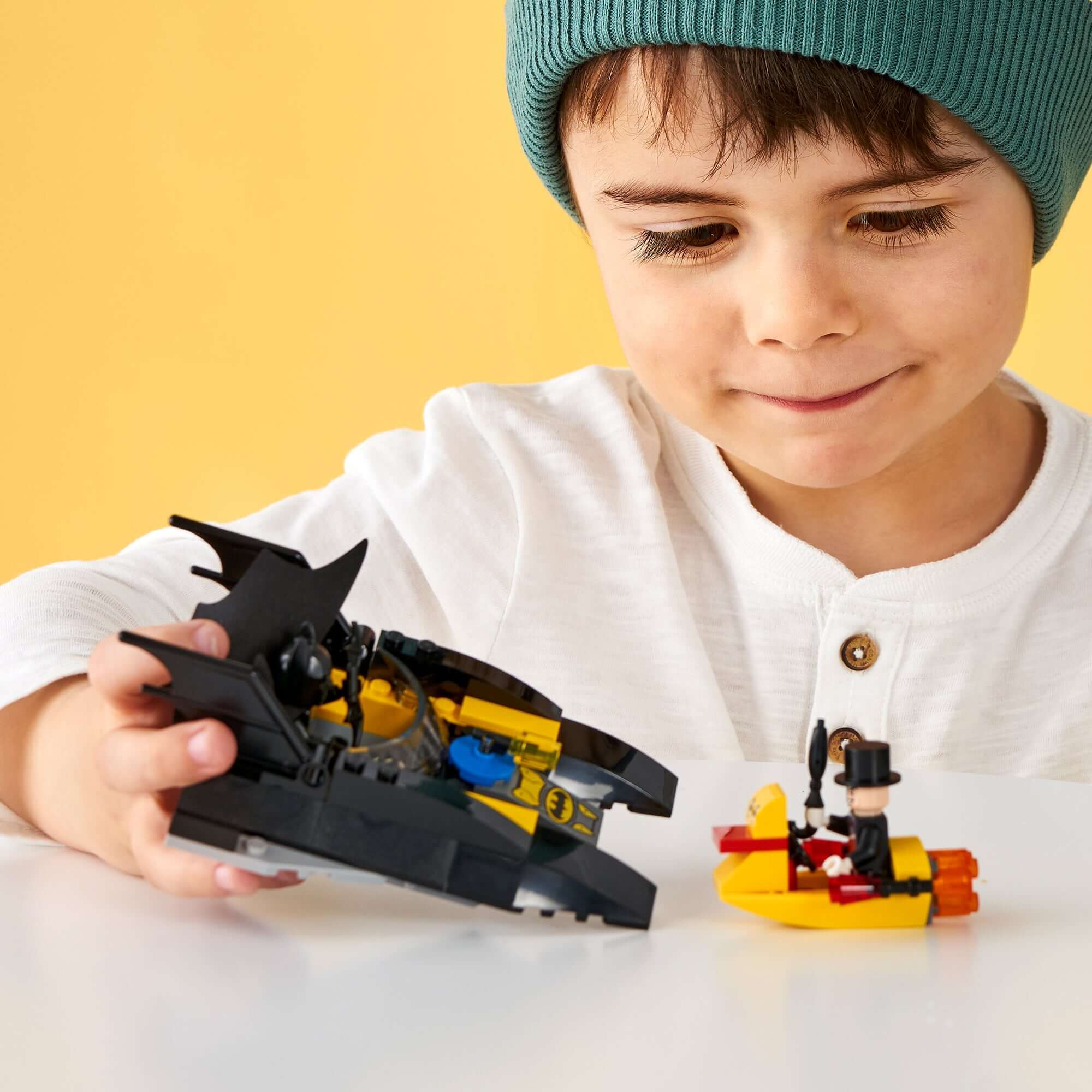 Child playing with LEGO® Batman Batboat and The Penguin mini-figures, showcasing creativity and fun.