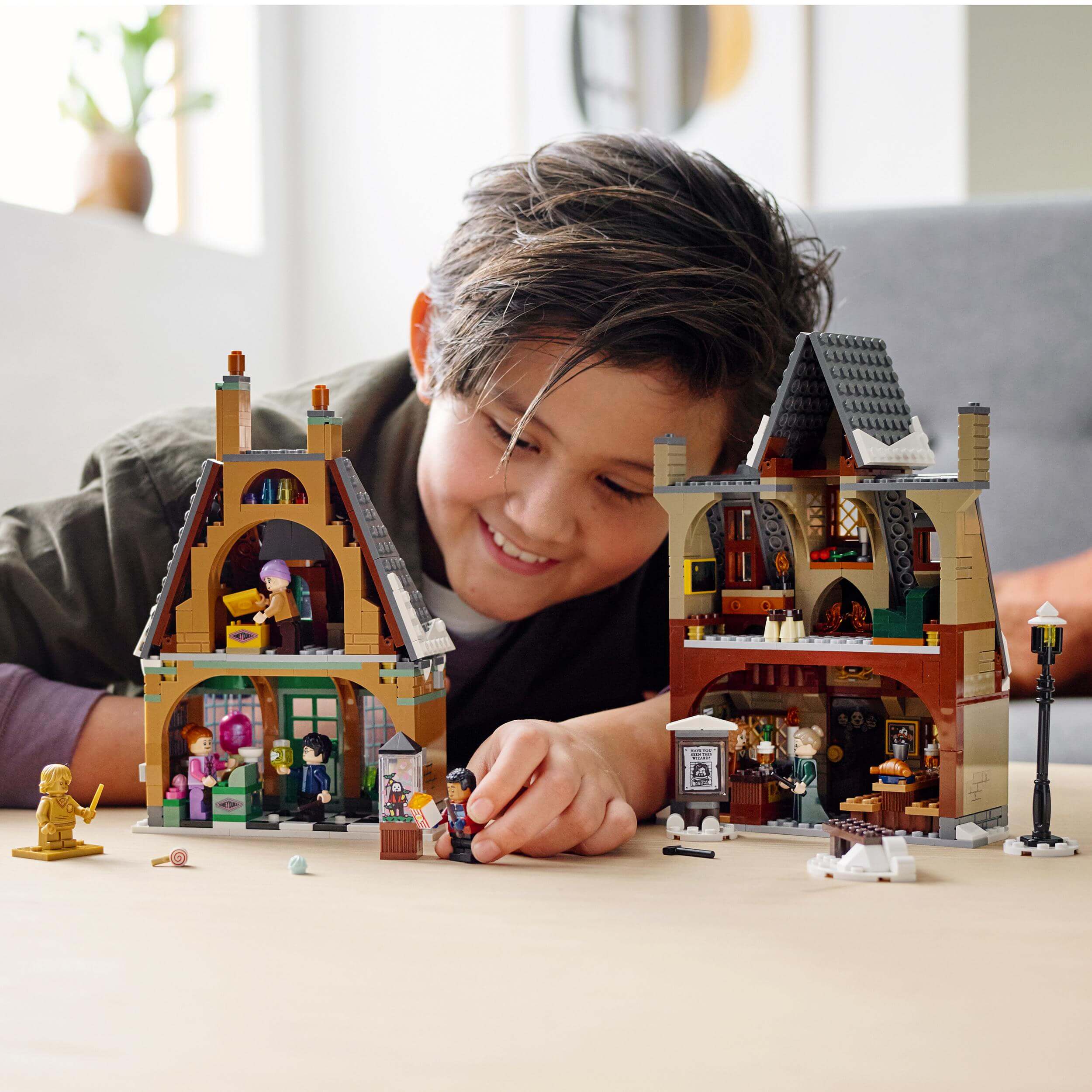 Child playing with LEGO® Harry Potter Hogsmeade Village Visit Set, featuring detailed shops and characters.