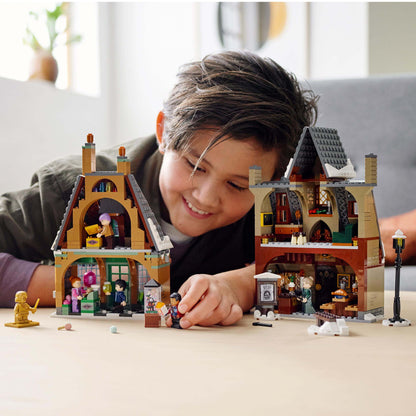 Child playing with LEGO® Harry Potter Hogsmeade Village Visit Set, featuring detailed shops and characters.