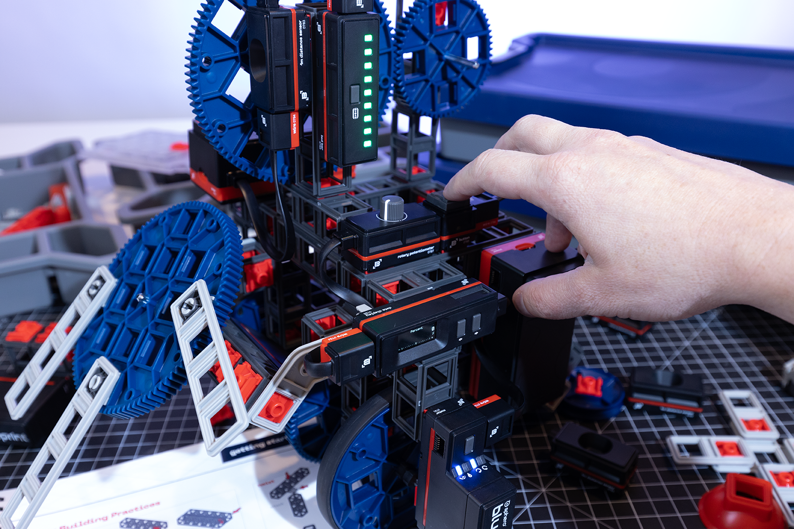 Hand interacting with a colorful mechanical construction set, featuring gears and modular components on a workspace.