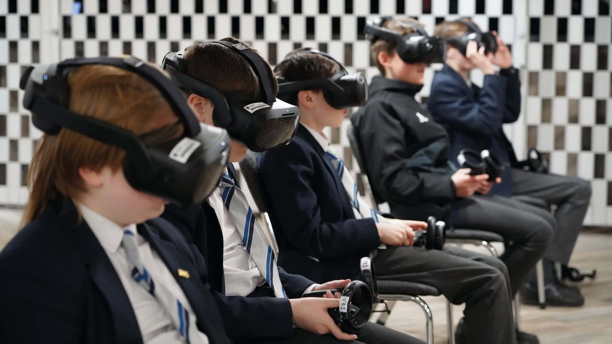 Students experiencing virtual reality technology in a classroom setting, wearing VR headsets and focused on gaming.