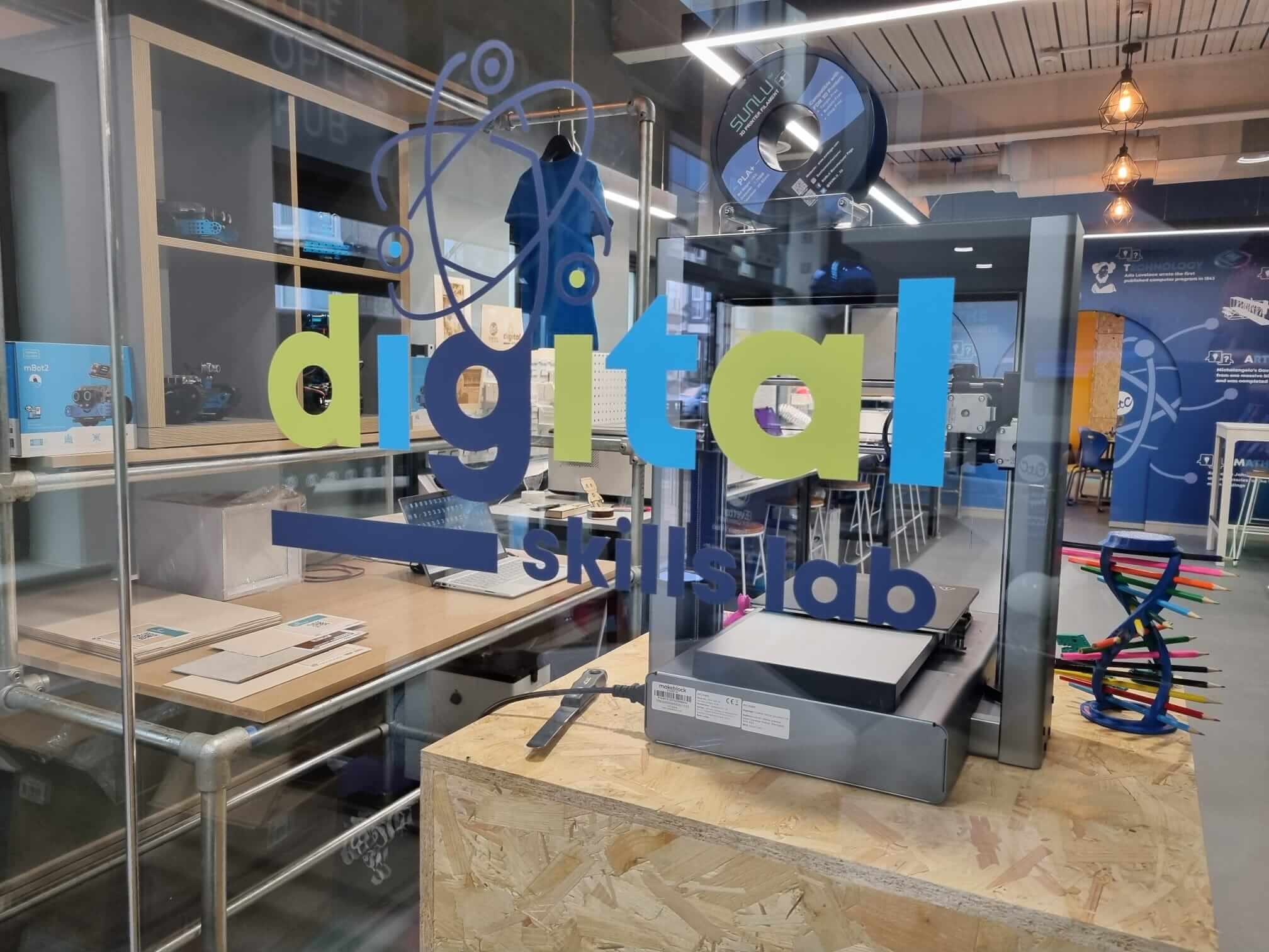 View of a digital skills lab featuring 3D printing equipment and a vibrant sign. Ideal for tech education and innovation.
