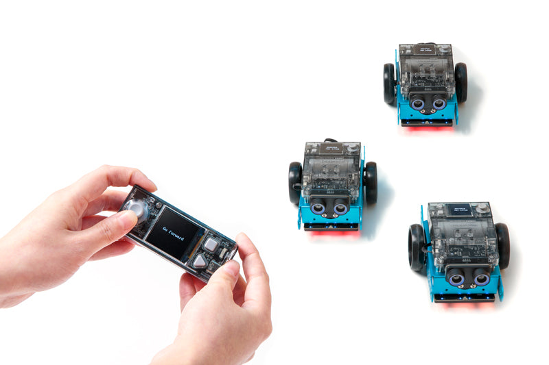 Hands using a smartphone to control three Makeblock mBot 2 educational robots on a white background.