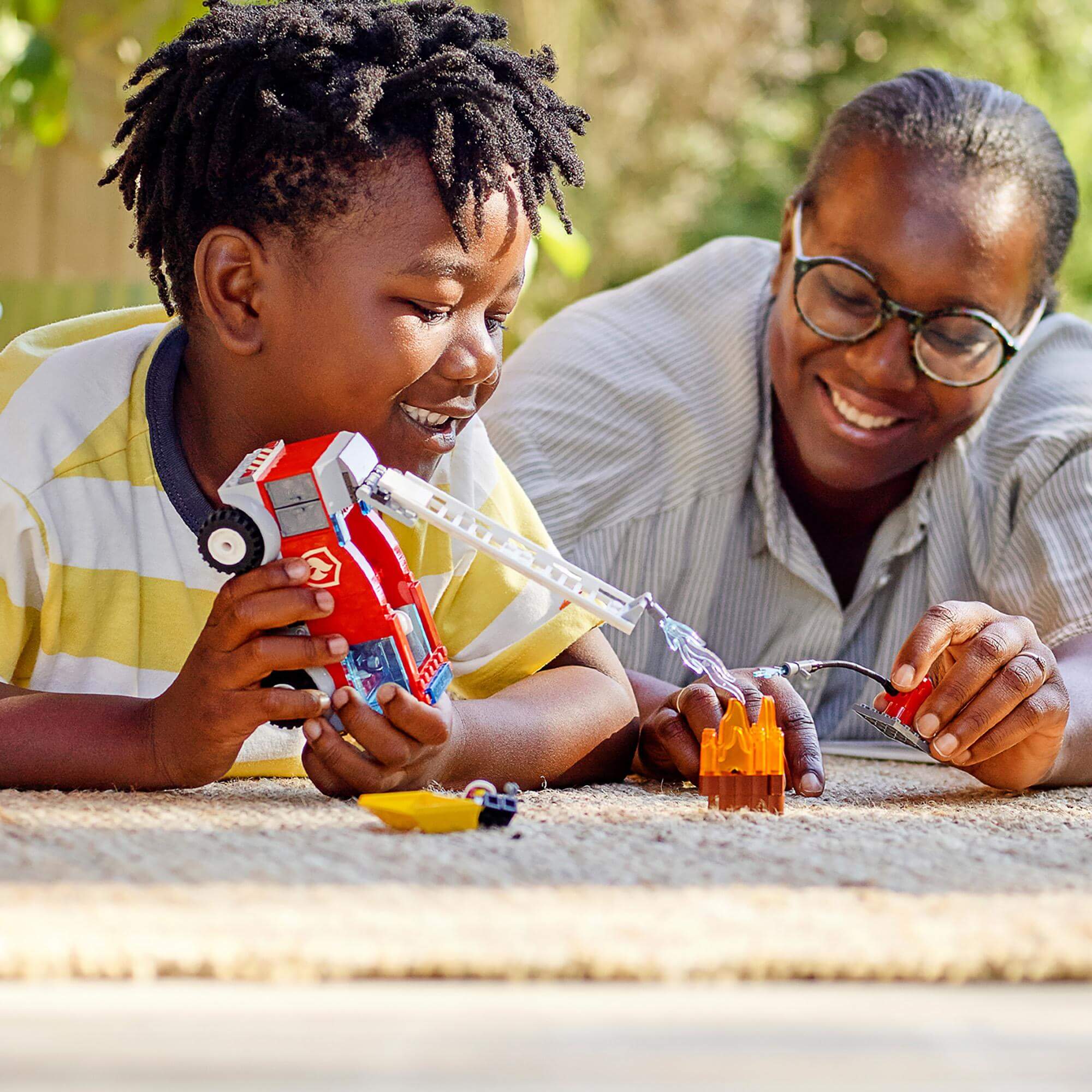 Child and adult playing with LEGO® City Fire Ladder Truck Toy 60280 on the floor, enjoying creative playtime together.