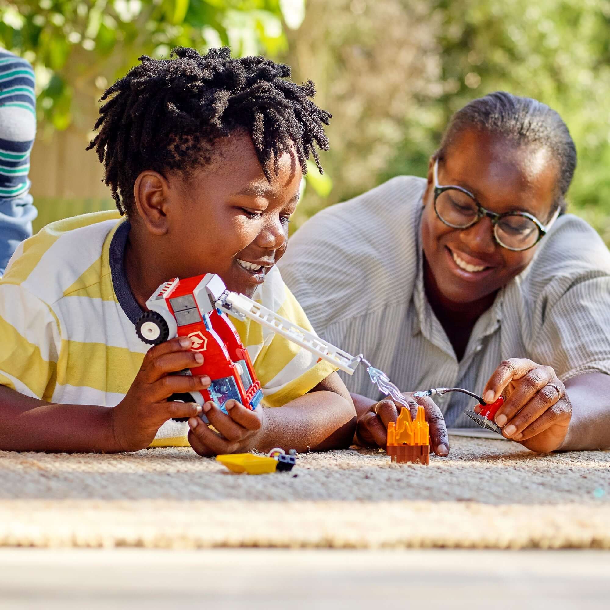 Child playing with LEGO® City Fire Ladder Truck Toy alongside a smiling adult, enjoying creative building fun.