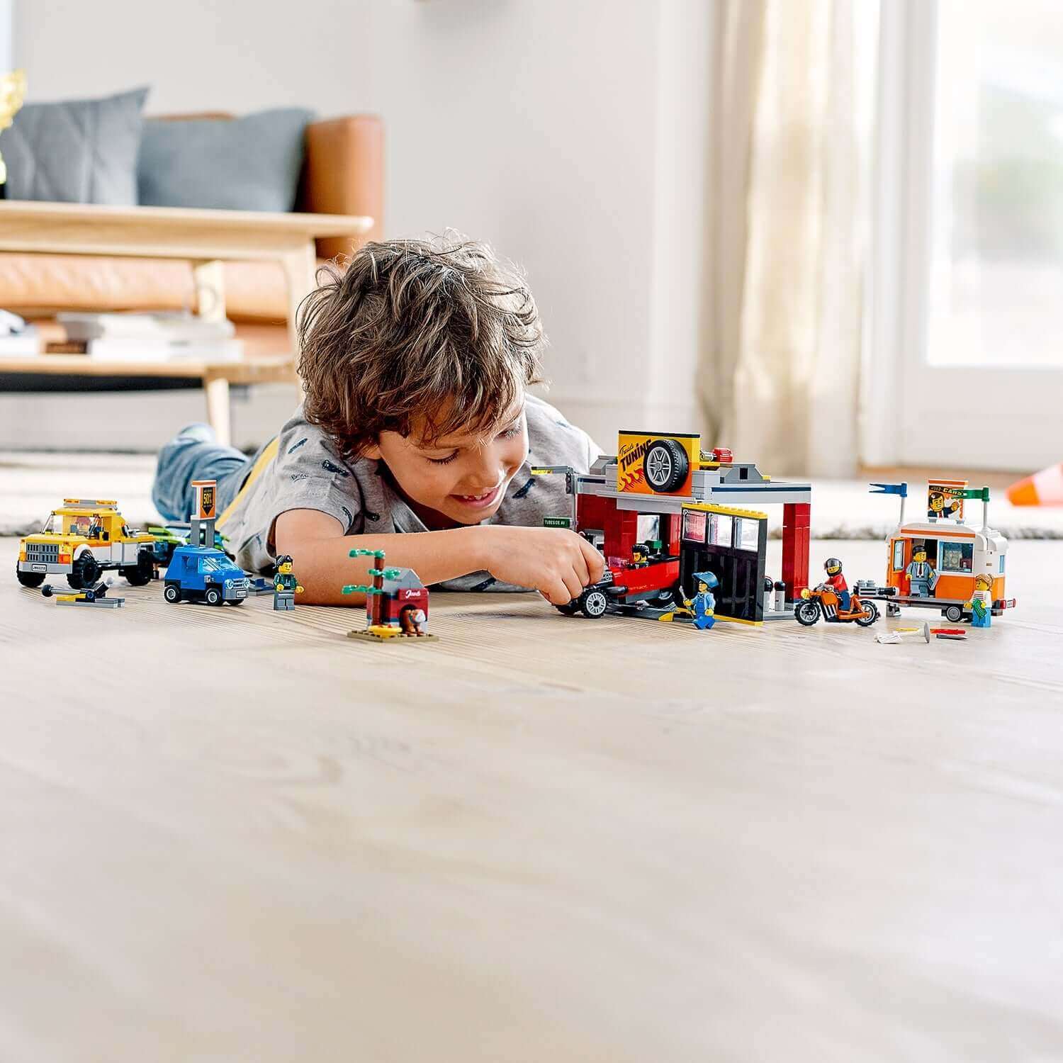 Child playing with LEGO® City Nitro Wheels Tuning Workshop set 60258, featuring vehicles and workshop scene.