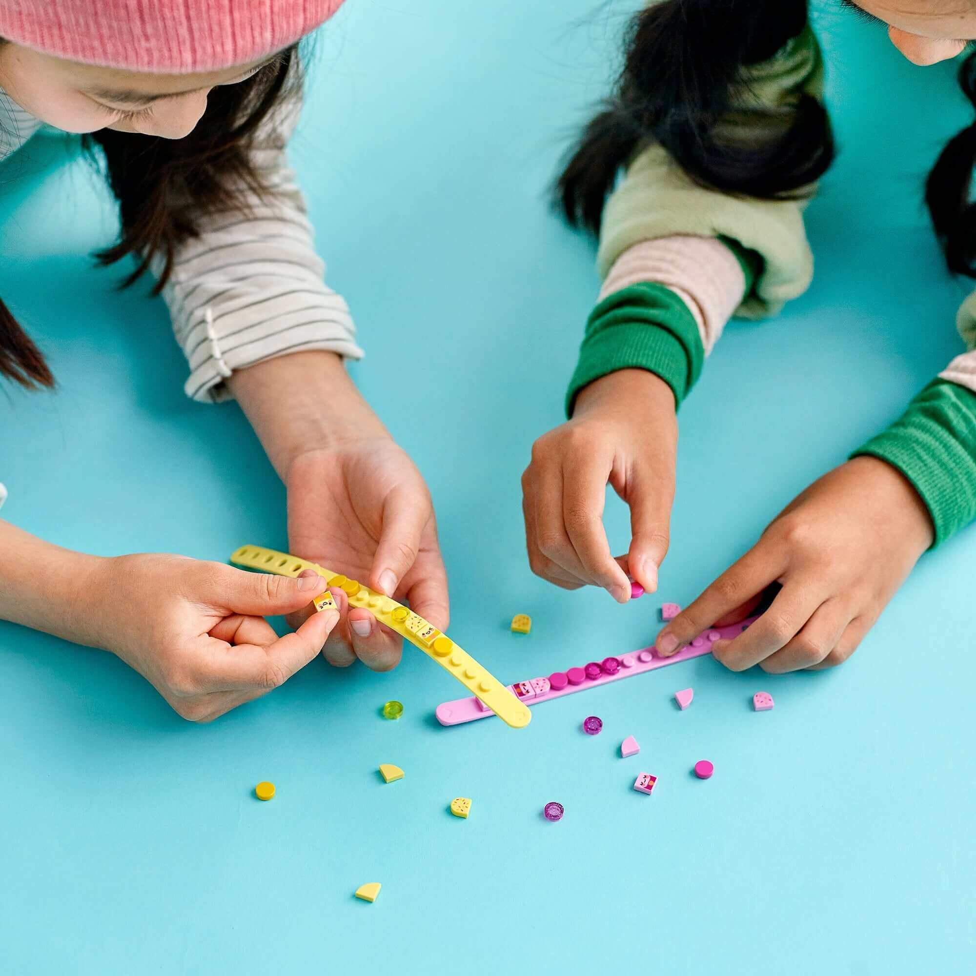 Kids creating colorful LEGO® DOTS Ice Cream Besties Bracelets with vibrant tiles on a blue background.