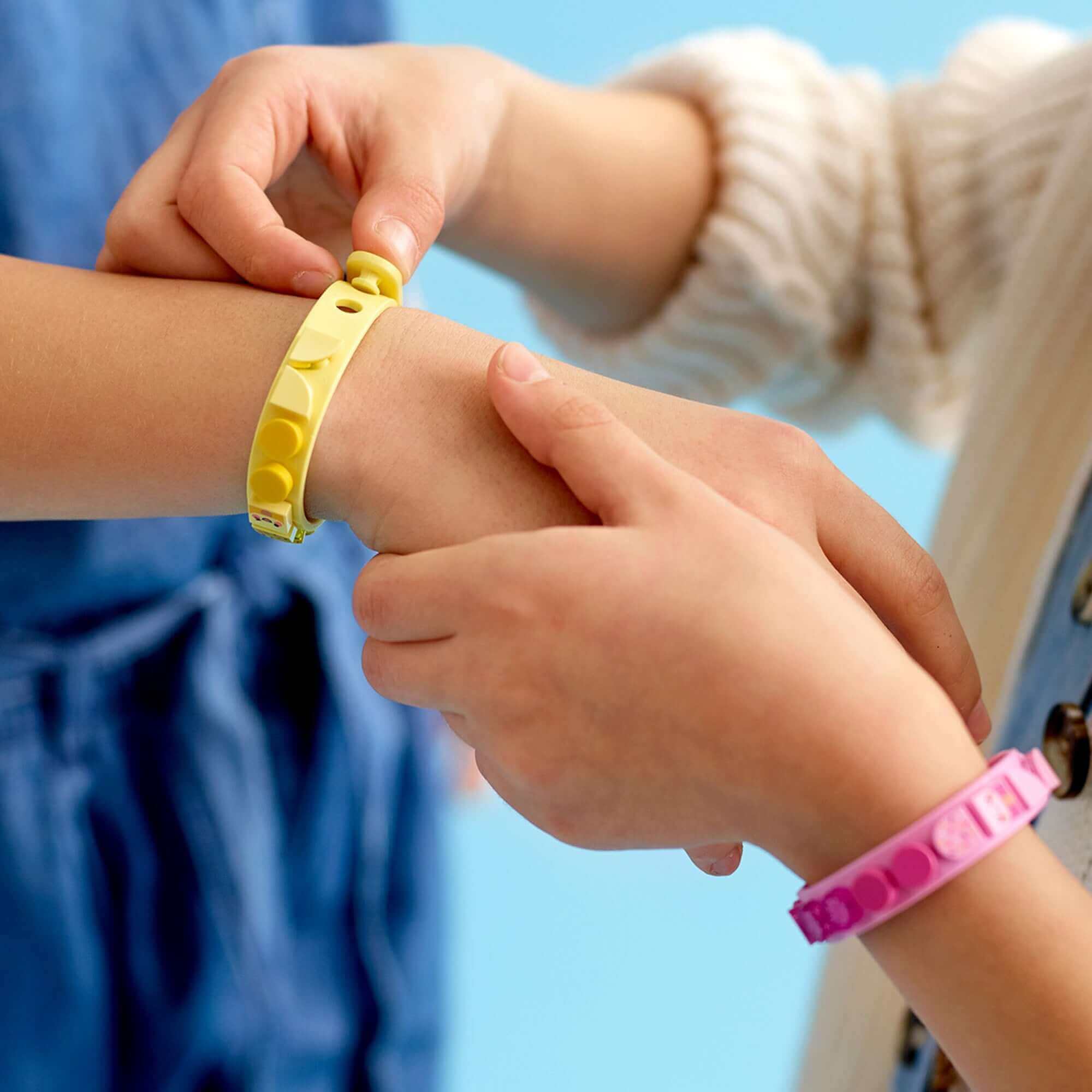 Two children adjusting LEGO® DOTS Ice Cream Besties Bracelets in yellow and pink with colorful tiles.