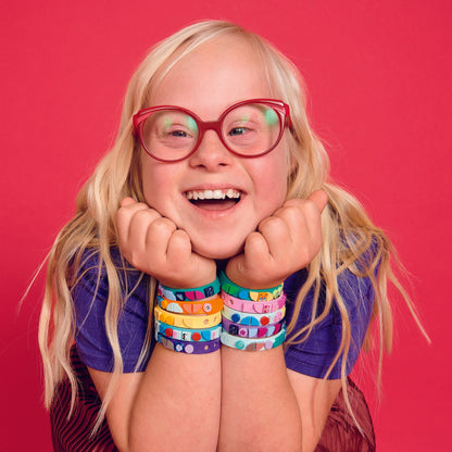 Child smiling with colorful LEGO® DOTS starlight bracelets on wrists against a vibrant pink background.