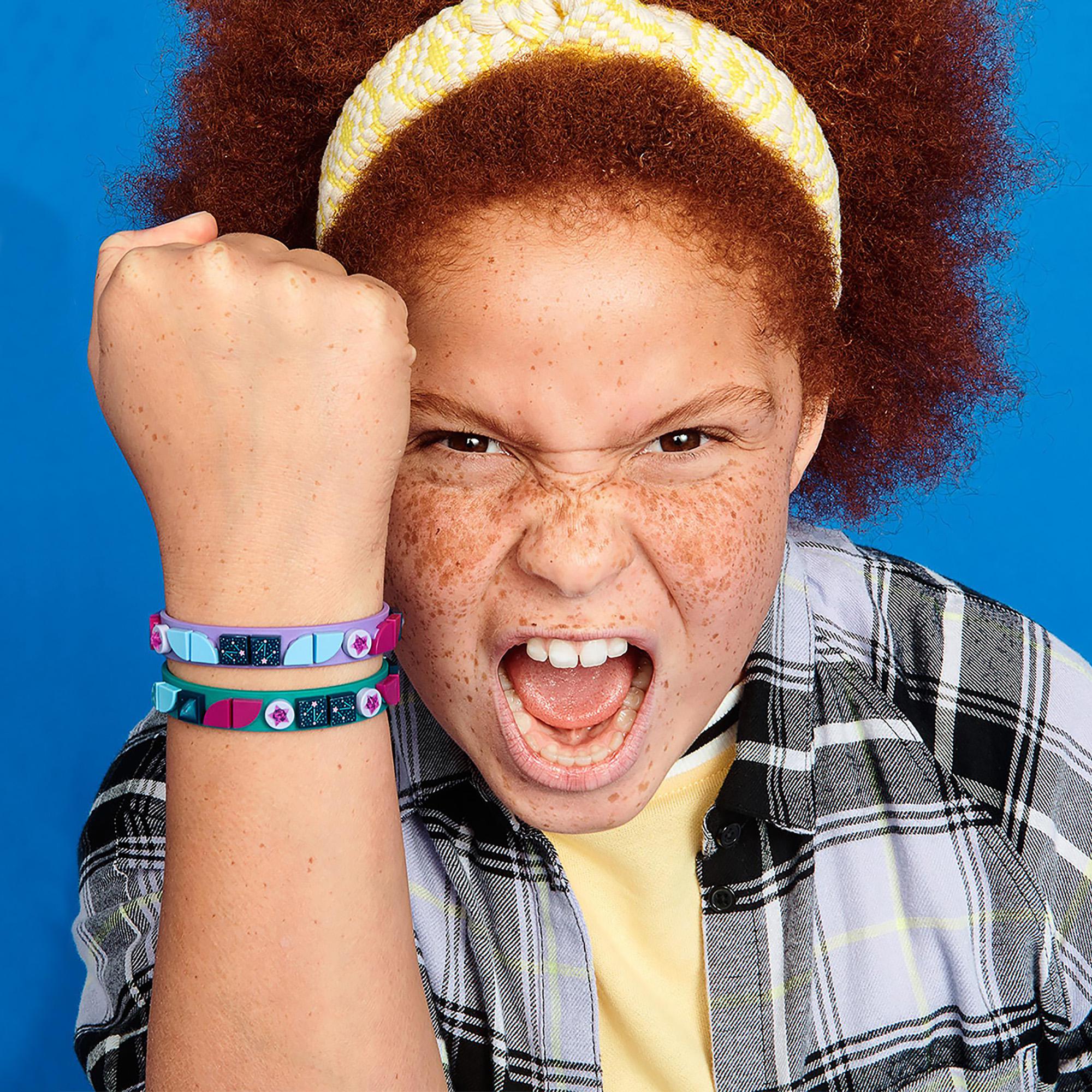 Child showing enthusiasm while wearing LEGO® DOTS Starlight Bracelets, featuring teal and purple designs.