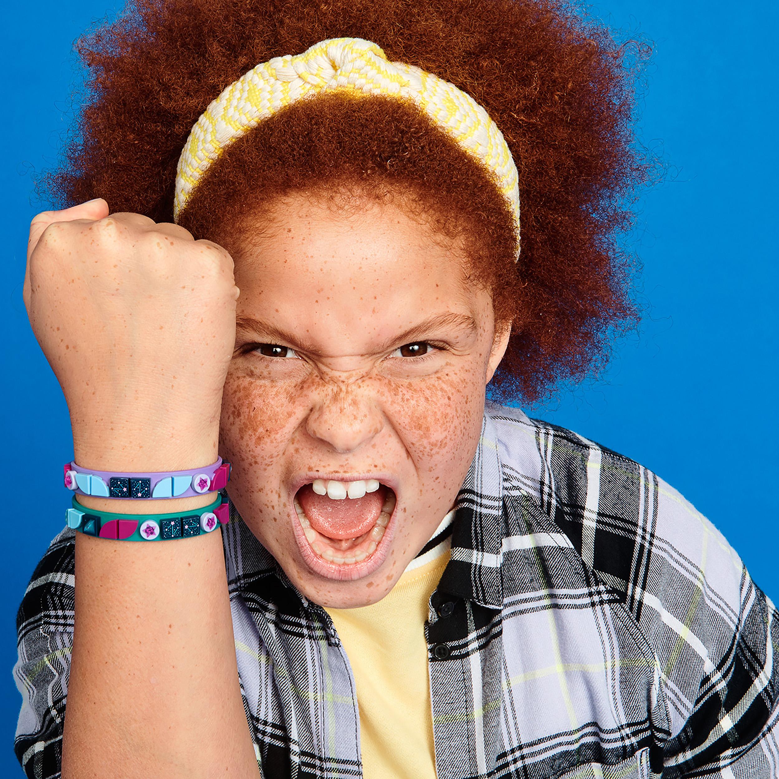 Child proudly showing off colorful LEGO® DOTS Starlight bracelets on wrist, expressing creativity and joy.