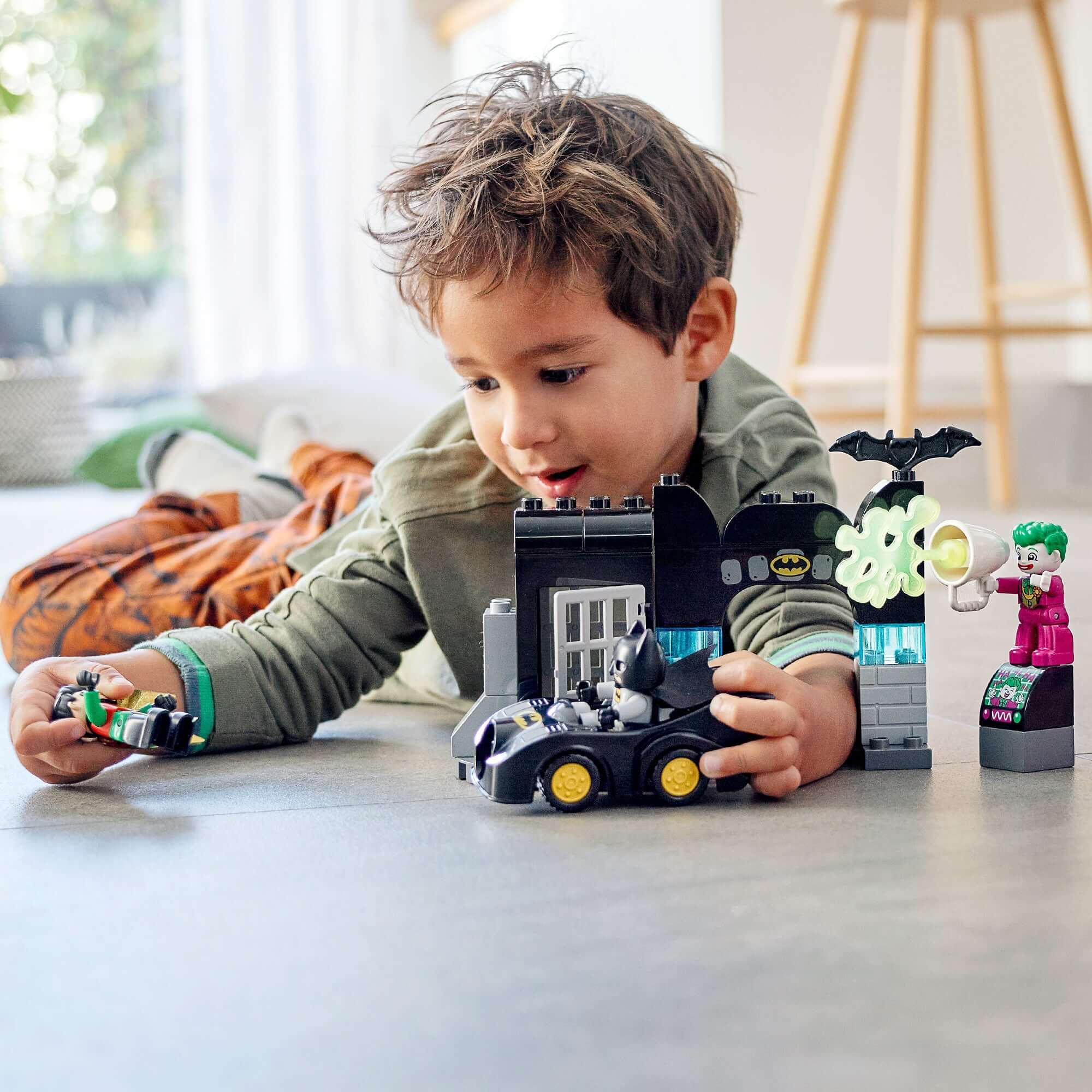 Child playing with LEGO® DUPLO Batman Batcave set featuring Batman, Robin, and THE JOKER.