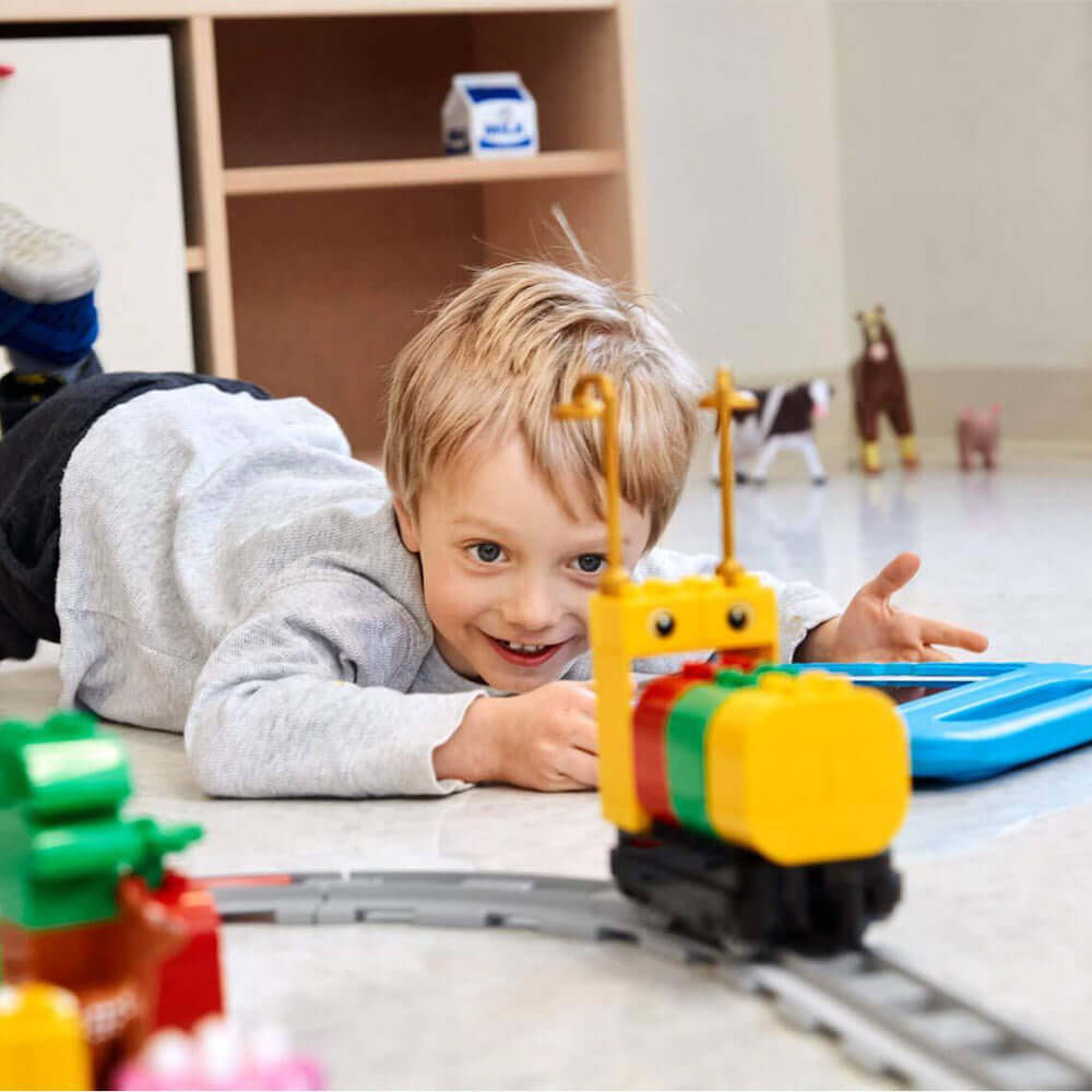Young child playing with LEGO Education Coding Express train on the floor, exploring coding concepts.
