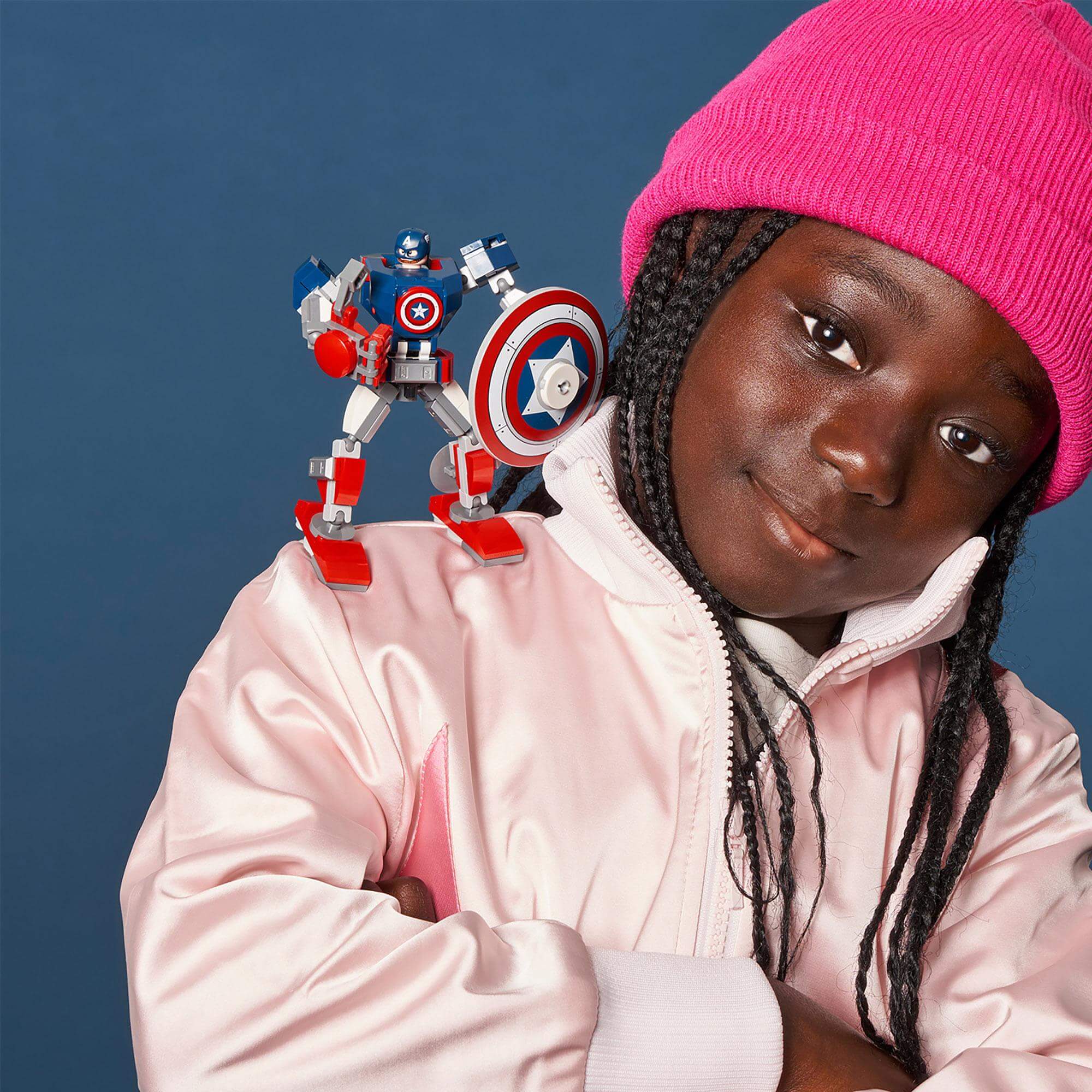 Child with a pink hat poses confidently with LEGO Marvel Avengers Captain America Mech toy on her shoulder.