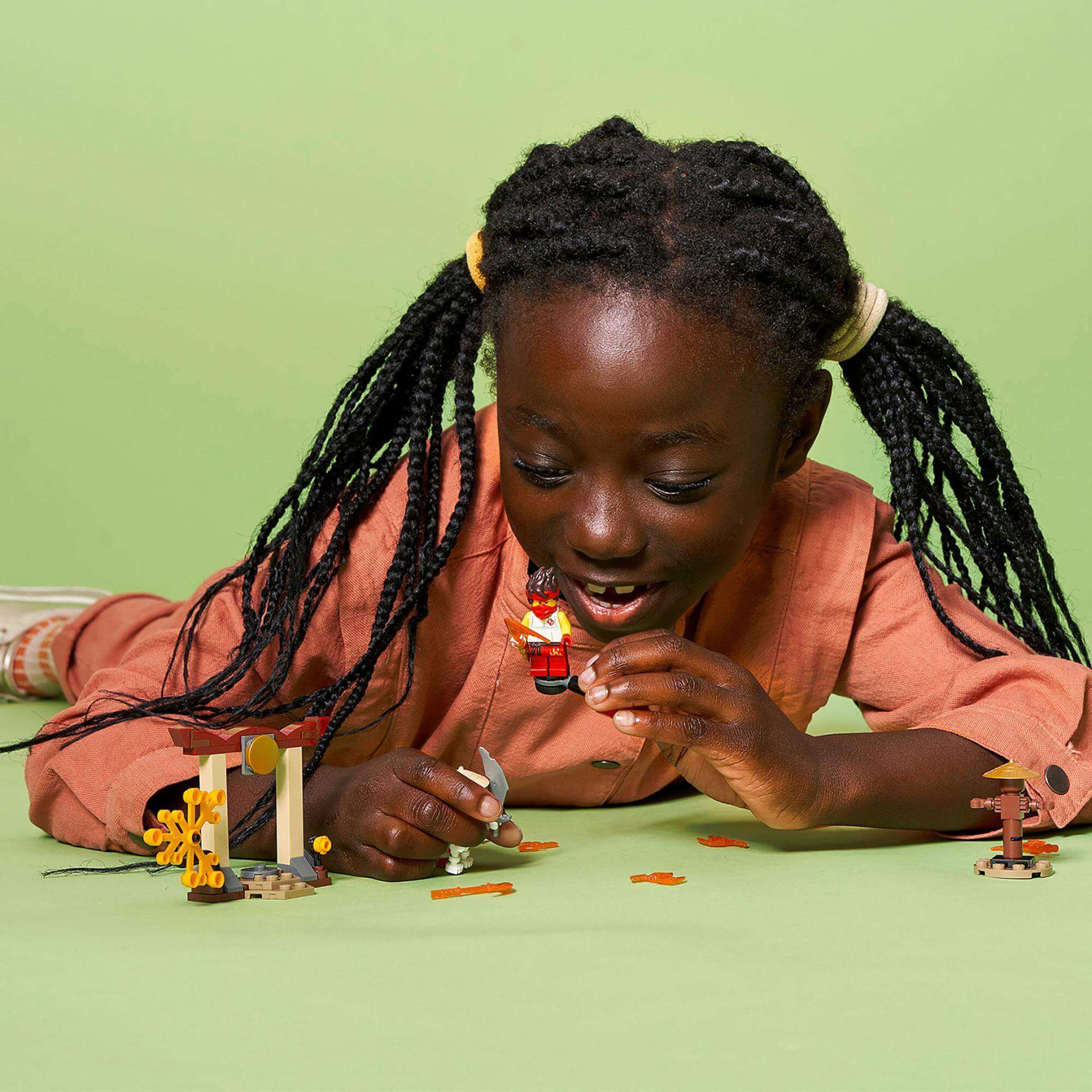 Child playing with LEGO® NINJAGO set, enjoying epic battles with Kai and Skulkin on a green background.