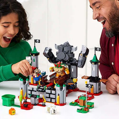 Child and adult enjoying LEGO® Super Mario™ Bowser's Castle Boss Battle Expansion set, featuring Bowser and interactive play.