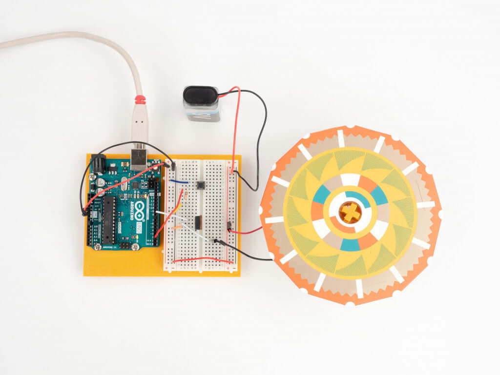 Arduino board setup with a sensor and colorful spinning disc for educational electronics project.