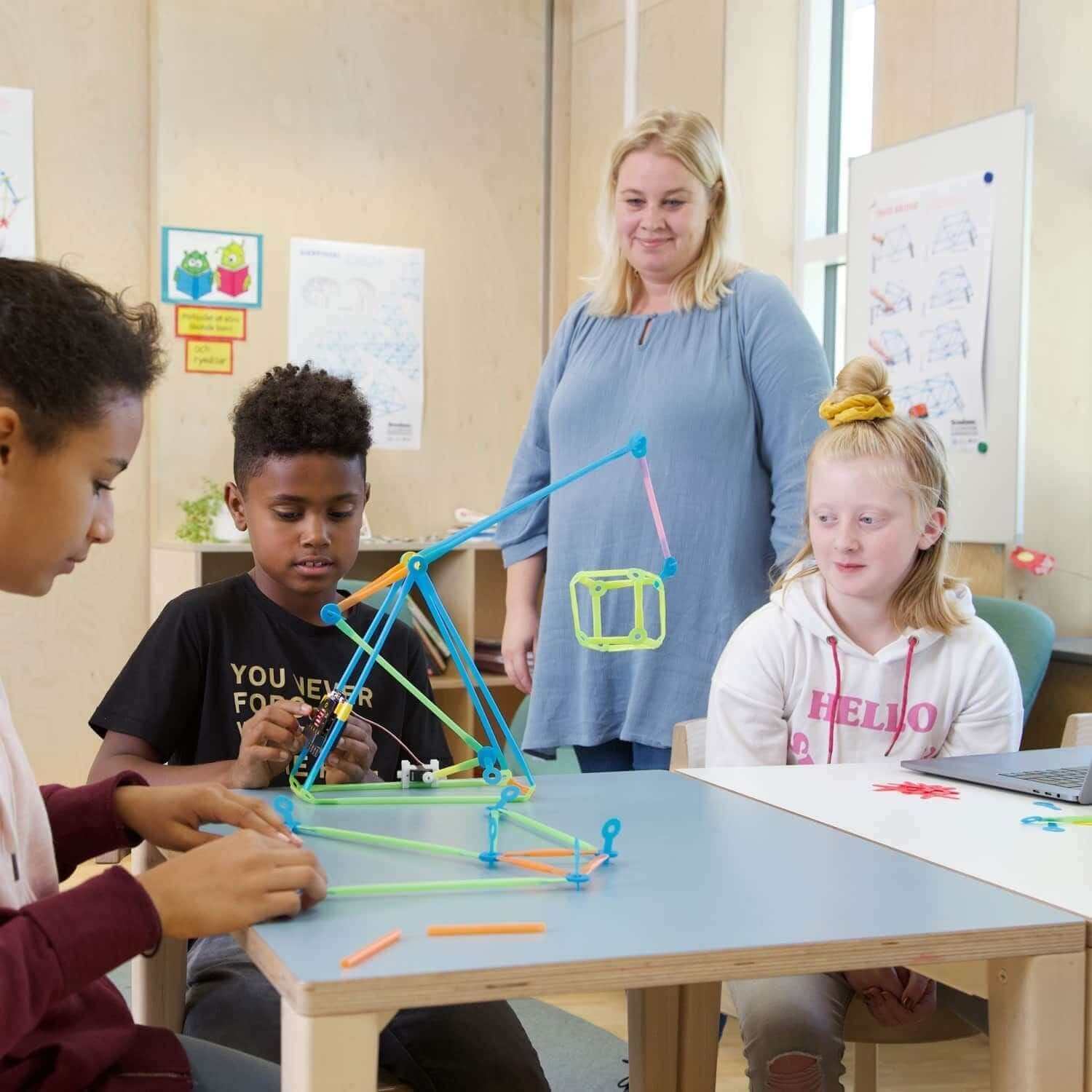 Kids building a robotic structure with Strawbees and micro:bit in a classroom, guided by a teacher.