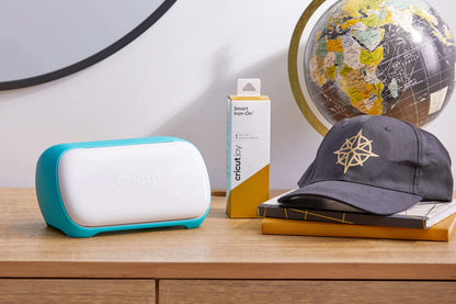 Cricut Joy cutting machine beside Smart Iron-On material and a custom hat on a wooden table.