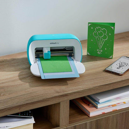 Cricut Joy cutting machine with green card in use, showcasing personalized greeting cards on a wooden table.