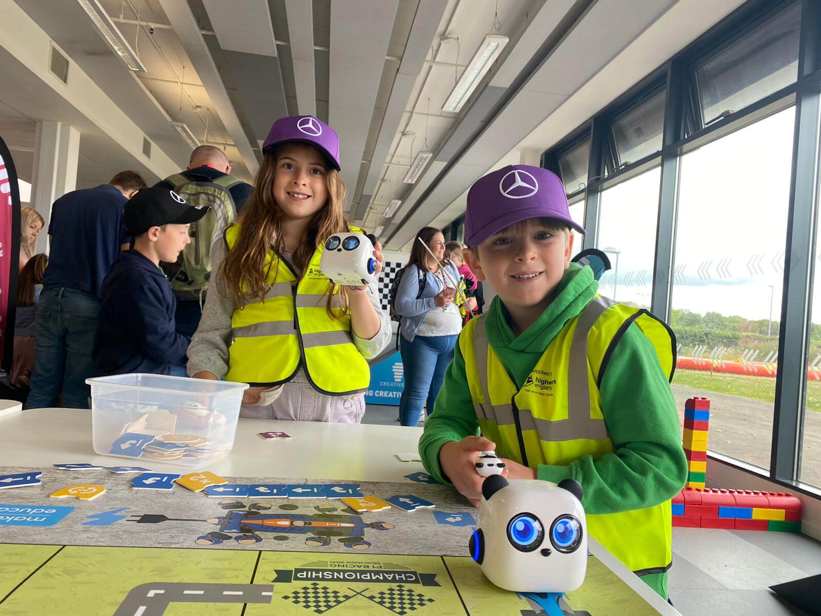 Children in safety vests enjoying a robotics activity, showcasing learning and fun at a tech event.