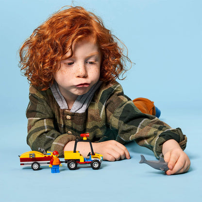 Child playing with LEGO® City Beach Rescue ATV toy set, featuring a lifeguard minifigure and a shark.