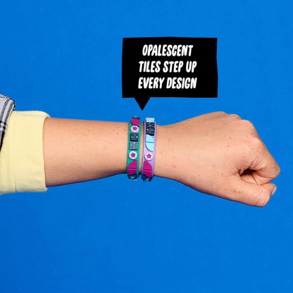 Child's hand showcasing LEGO® DOTS Starlight Bracelets with opalescent tiles on a vibrant blue background.