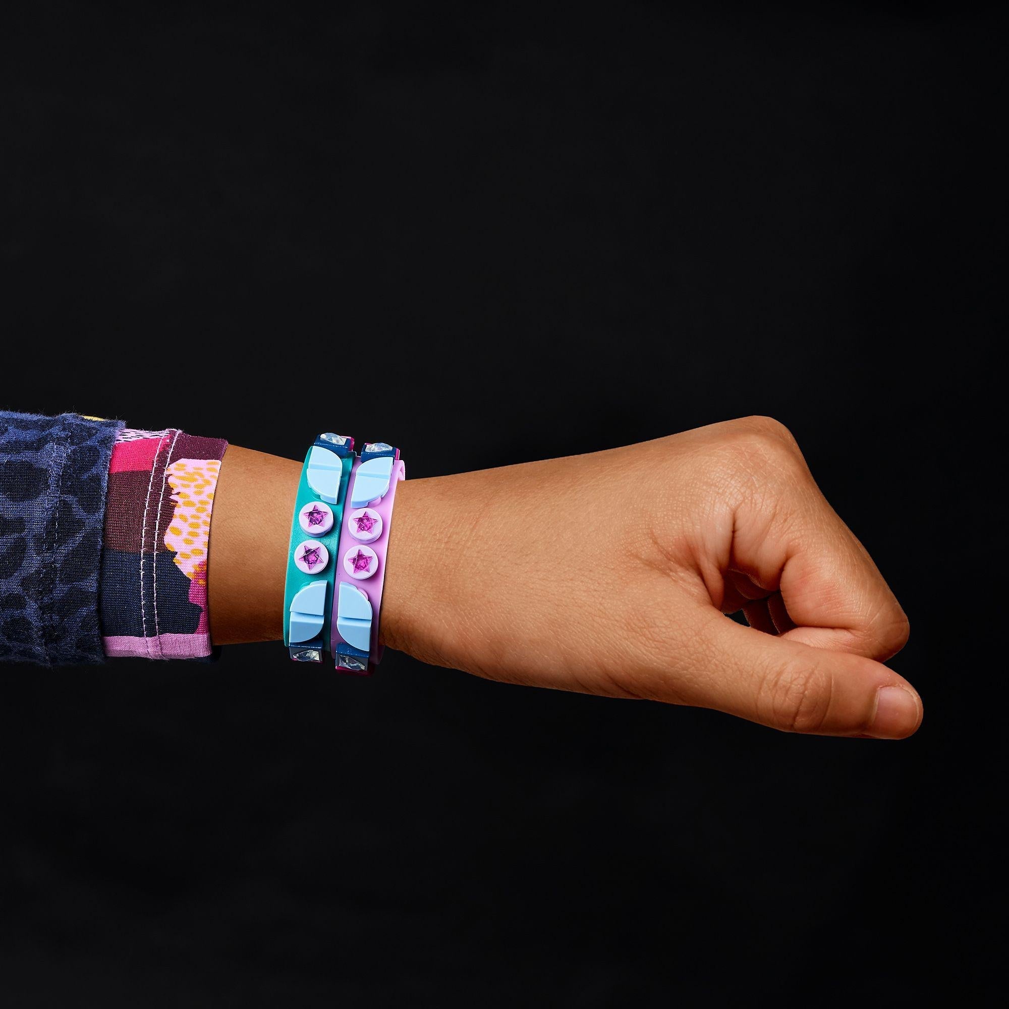 Child's hand adorned with teal and purple LEGO® DOTS Starlight bracelets showcasing creative tile designs.
