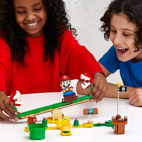 Two children enjoy the LEGO® Super Mario™ Piranha Plant Power Slide set, featuring Mario on a seesaw with Piranha Plants.