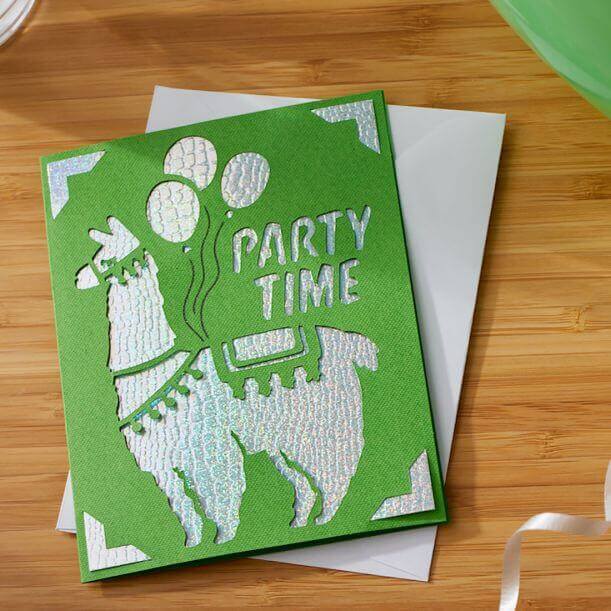 Green party invitation card featuring a llama with balloons and the text 'Party Time', set on a wooden surface.