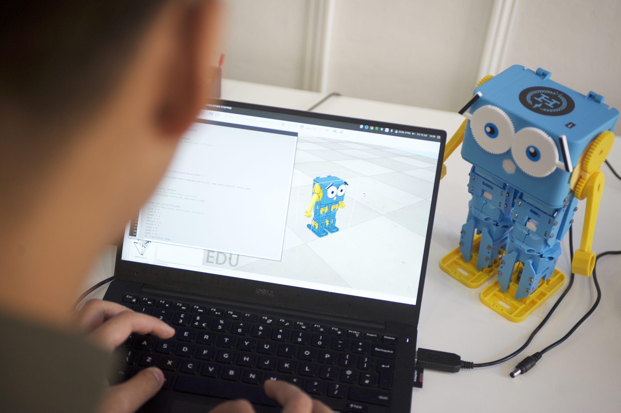 Child coding on a laptop with the Marty V2 walking robot beside it, showcasing interactive learning.