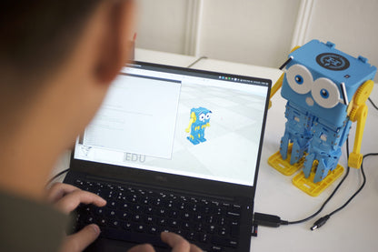Child coding on a laptop with the Marty V2 walking robot beside it, showcasing interactive learning.